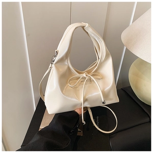 Detail of a creamy white leather handbag featuring a delicate bow and silver metal beads