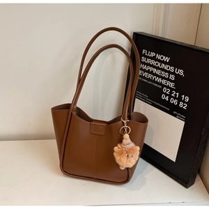 Detail of caramel leather tote bag with vertical stitching and pink plush charm