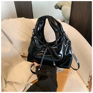 Detailed view of black patent leather hobo bag with bow accent on beige trench coat