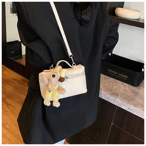 Detail of cream box bag with lychee texture leather and a cute plush dog pendant