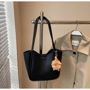 Detail of a black bucket tote bag with a cute plush charm hanging on a rack