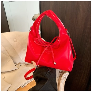 Detail of red glossy handbag featuring a leather bow and polished silver bead accents