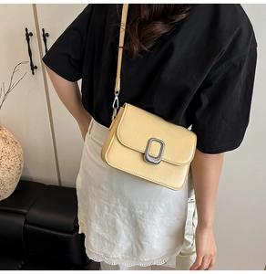 Close-up of pale yellow crossbody bag featuring a silver metal buckle and smooth finish
