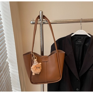 Detail of caramel brown leather tote bag with decorative stitching and cute teddy bear charm