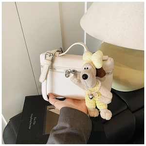 Close-up of a white lychee grain leather box bag with silver zippers and a cute plush charm