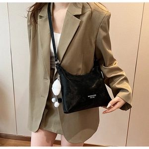 Detail of black textured PU leather crossbody bag with white plush ball charm accessory