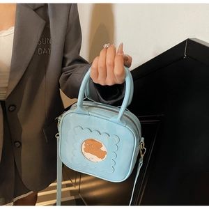 Close-up of light blue patent leather bag with cartoon bear window detail and top handle