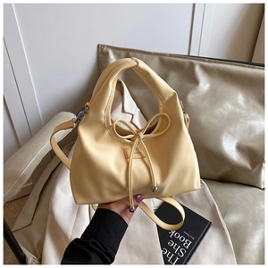 Detail of butter yellow crossbody bag with bow drawstring and brand label on matte leather