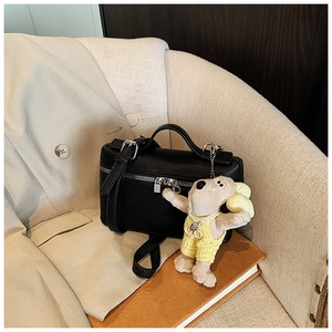 Detail of black pebbled leather box bag with a cute plush charm on a beige sofa