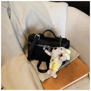 Detail of black pebbled leather box bag with silver zipper and cute plush dog charm