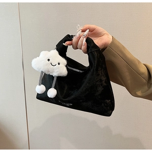 Detail of a black velvet handbag featuring a cute white cloud plush charm with smiley face