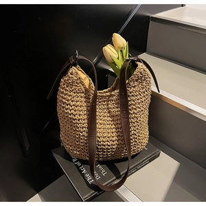 Dettaglio borsa in paglia intrecciata con manici in pelle marrone e anelli metallici