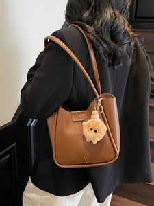 Brown vintage leather tote bag with plush charm shown on a shoulder in a stylish setting