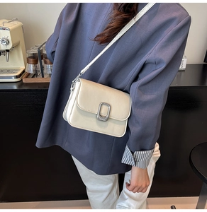 Detail of a beige flap crossbody bag with crocodile texture and silver U-shaped buckle