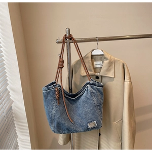Close-up of blue washed denim tote bag featuring brown rope handles and silver metal detail