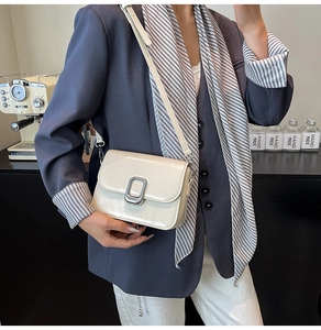 Chic off-white glossy leather crossbody bag with silver buckle on a stylish model