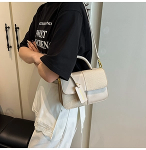 Detail of cream crossbody bag with woven texture and smooth leather flap on a model