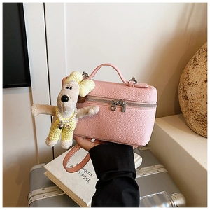 Detail of pink lychee leather handbag with cute plush dog pendant and silver zippers