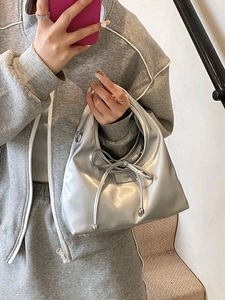 Silver metallic crossbody bucket bag with bow detail held by model on minimalist stairs