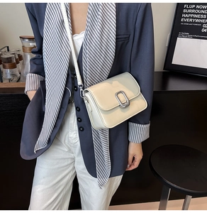 Detail of a minimalist cream flap bag with silver buckle and leather shoulder strap
