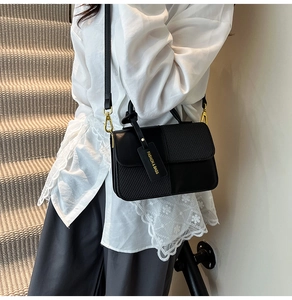 Detail of black crossbody bag with mixed leather textures and golden hardware on model