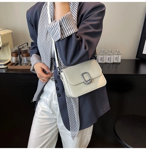 Beige PU leather crossbody bag with silver buckle worn by a model in a cafe