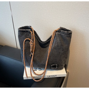 Detail of dark denim tote bag featuring contrasting orange rope handles and side knots