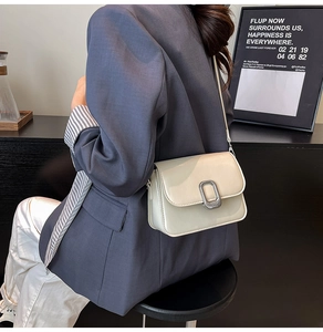 Detail shot of off-white crossbody bag with silver buckle worn on a blue suit jacket