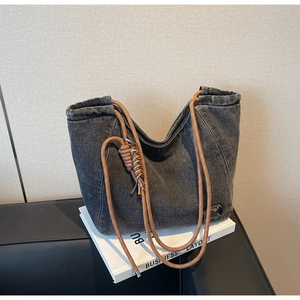 Detail of a grey denim tote bag featuring woven rope straps and washed texture