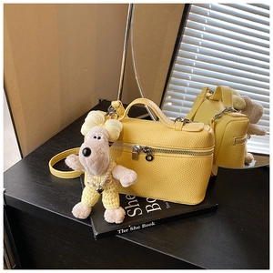 Detail of yellow box handbag with lychee grain texture and cute plush puppy charm