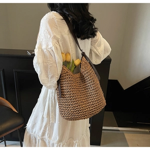 Dettaglio di una borsa hobo in paglia con tracolla in pelle e tulipani
