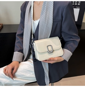Detail of minimalist cream leather crossbody bag with iconic brushed metal rectangle buckle