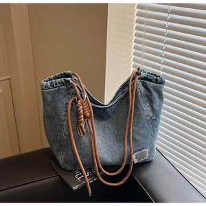 Detail of blue denim tote bag featuring woven rope straps and a knotted tassel pendant