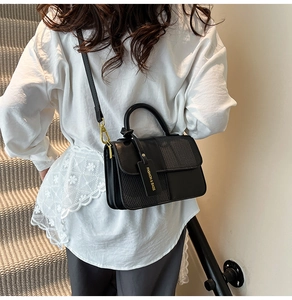 Detail of black crossbody bag featuring textured weave panels and a branded hangtag
