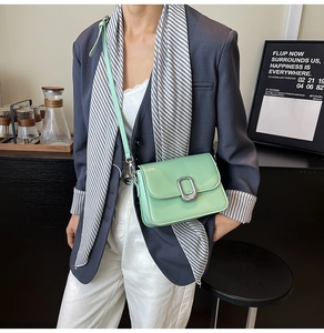 Polished light green crossbody bag with silver buckle worn by model in urban setting