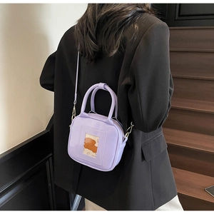 Detail of purple patent leather crossbody bag featuring a cute dog card slot on model