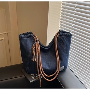 Detail of blue denim tote bag with brown woven rope handle and distressed patch on leather sofa