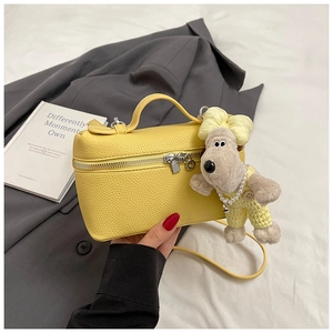 Detail of yellow lychee leather handbag featuring a cute plush dog charm accessory