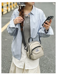 Detail shot of a beige nylon mini crossbody bag featuring adjustable black straps and pockets