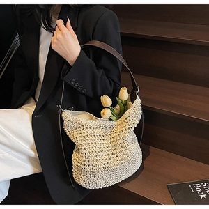 Dettaglio di una borsa tote in paglia beige con tracolla in pelle marrone indossata da una modella
