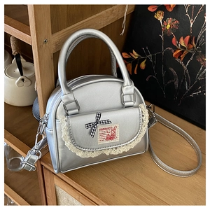 Detail of silver Boston bag featuring lace trim, plaid bow, and fantasy rabbit patch