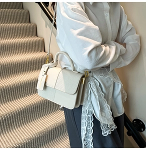 Detail view of cream crossbody bag with lizard pattern flap and golden hardware accents