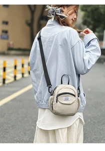 Close-up of stylish off-white canvas crossbody bag with black adjustable strap outdoors