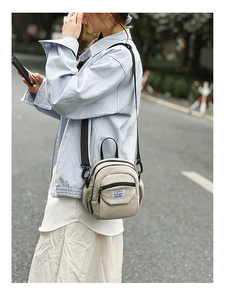 Detail view of a compact beige nylon crossbody bag with adjustable black strap and logo