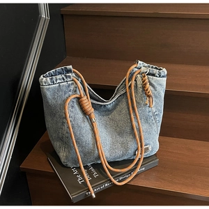 Detail of vintage washed denim tote bag with brown thick rope handles on wooden stairs