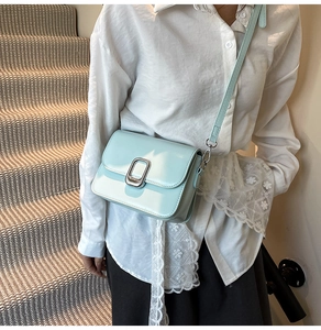 Detail of light blue patent leather small square bag with silver buckle on a model