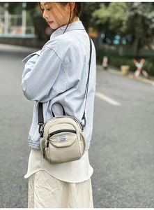 Close-up of minimalist beige nylon crossbody bag with black zipper and woven brand tag