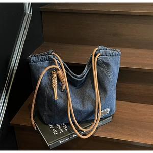 Detail of blue denim tote bag with thick braided rope handles and woven tassel charm