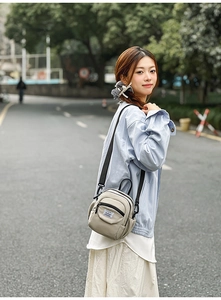 Outdoor shot of a beige canvas crossbody shell bag with black straps on a female model