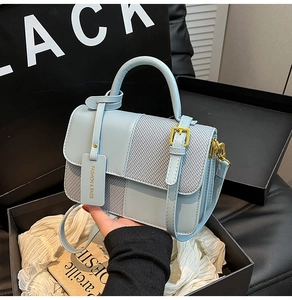 Close-up of light blue contrast handbag in a black gift box with woven texture detail